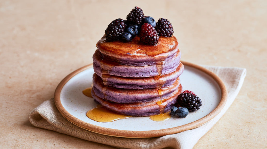 Pile de pancakes violets à l'ube nappés de sirop d'érable et garnis de fruits rouges.