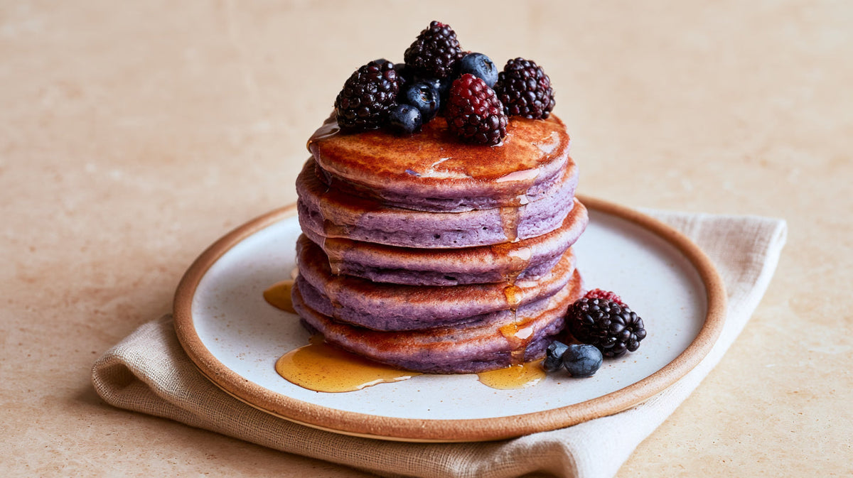 Pile de pancakes violets à l'ube nappés de sirop d'érable et garnis de fruits rouges.