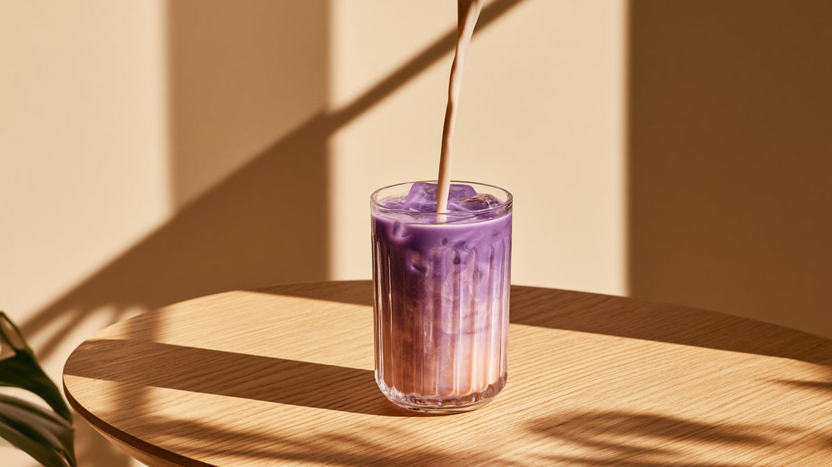Latte glacé à l'ube avec un dégradé naturel de violet et de lait dans un verre transparent.