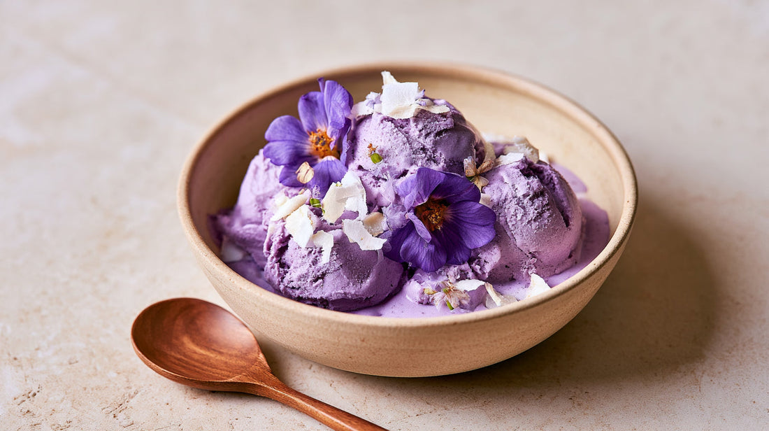 Nice cream vegan à l'ube servie dans un bol avec noix de coco râpée et fleurs comestibles.