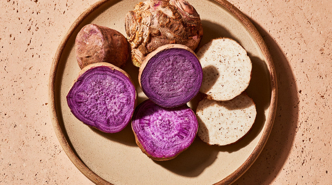 Comparaison entre une racine d'ube violette et une racine de taro coupées en deux sur une surface en pierre naturelle.
